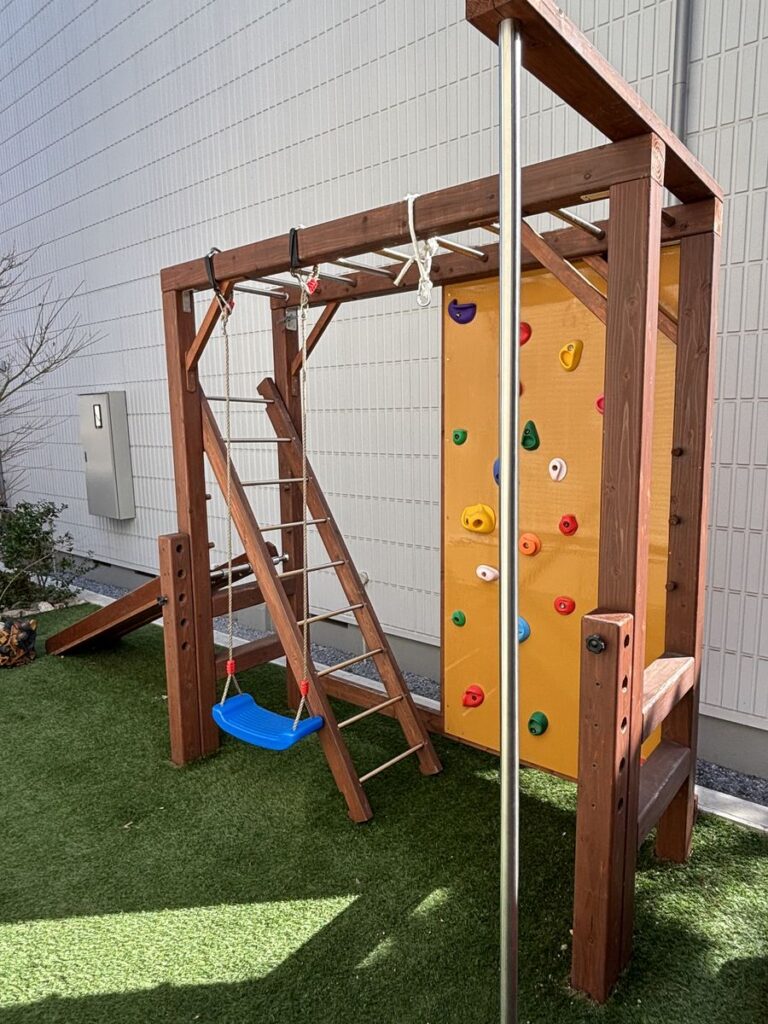 屋外の遊具。はしごやブランコ、ボルダリングの壁がある