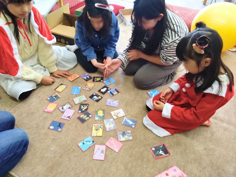 子どもたちが床に座ってカードを並べて遊んでいる